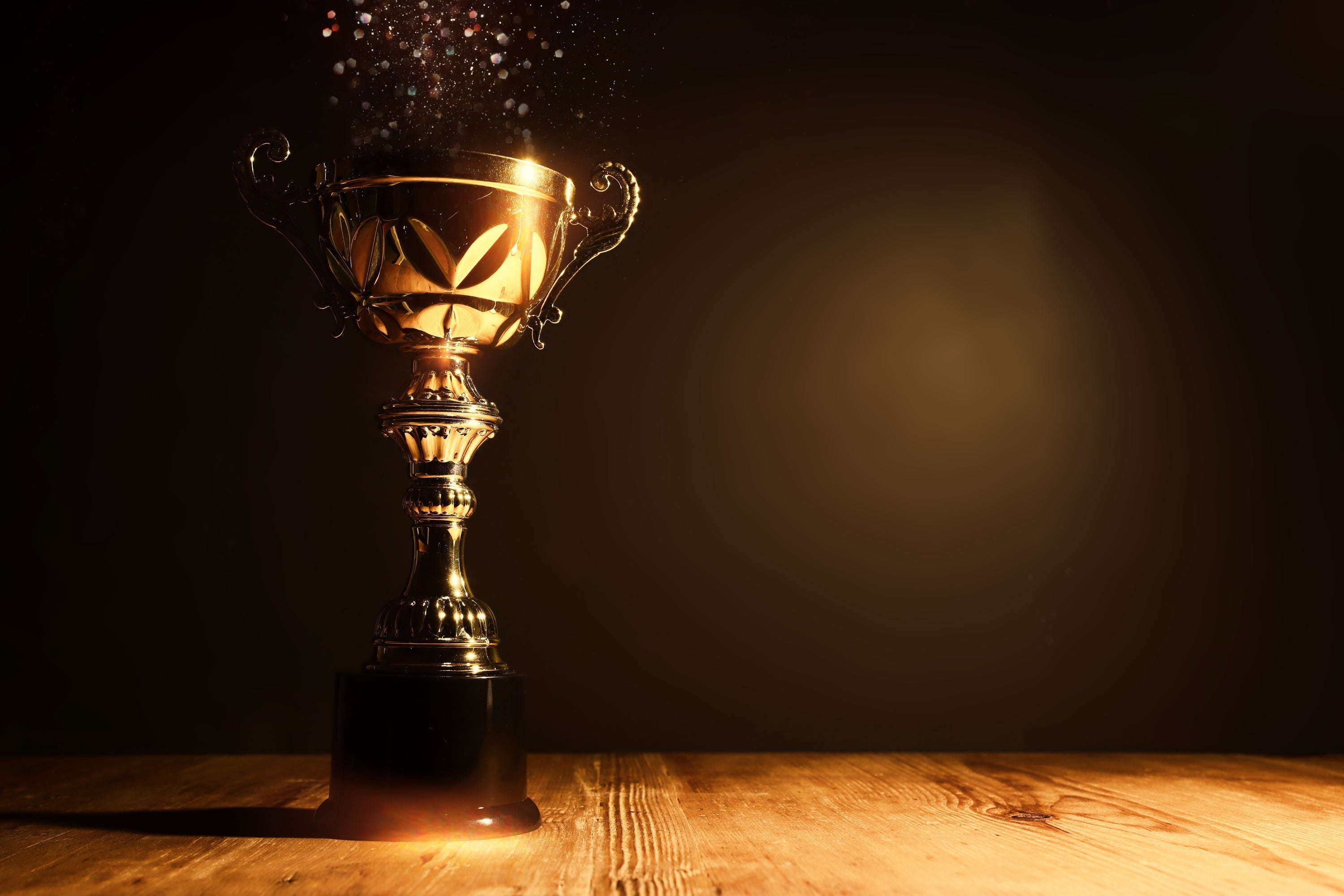 Glowing gold trophy on wooden surface for end of season sports awards ceremony - championship award with dramatic lighting and celebratory sparkles.