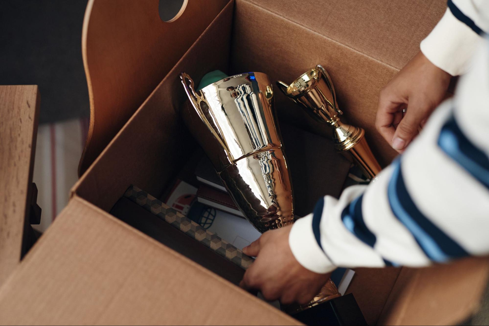 Box of old childhood trophies and medals being sorted during a home declutter session.